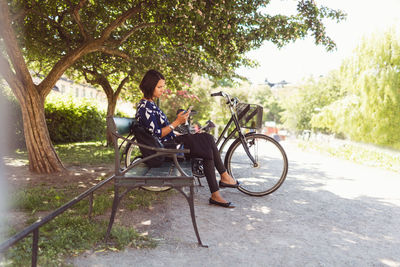 Side view of businesswoman using smart phone while sitting on park bench