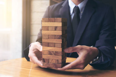 Midsection of businessman playing with wooden toy blocks at table