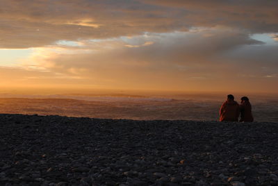 Rear view of man walking on beach against sky during sunset