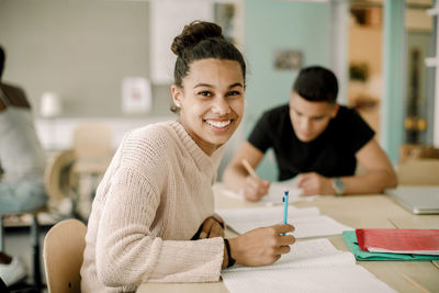 Portrait of smiling teenage girl studying while sitting in classroom