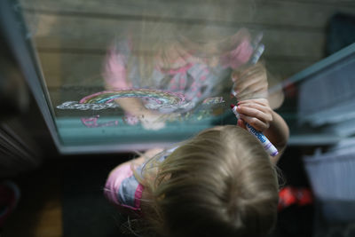 Above view of child drawing on window with markers