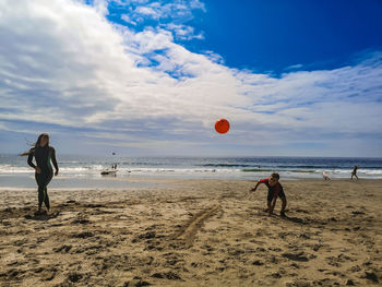 People playing with ball on beach against sky