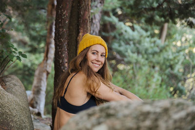 Portrait of smiling young woman against tree trunk
