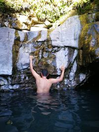 Rear view of shirtless man climbing rocks in forest