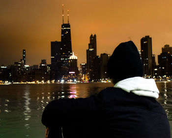 Rear view of man looking at illuminated city buildings at night