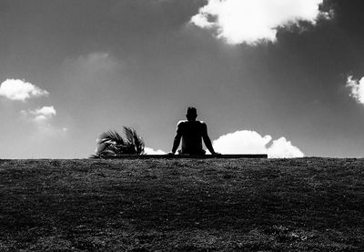 Rear view of men sitting on field against sky