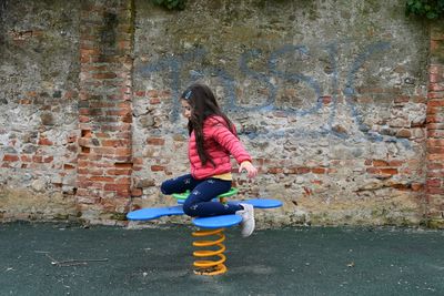 Side view of girl playing on spring ride against old wall