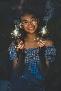 Portrait of young woman holding sparklers at night