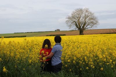 Rear view of couple standing amidst plants against cloudy sky