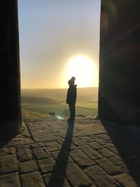 Side view of silhouette man standing against sun during sunset