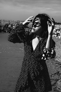 Young woman standing at beach against sky