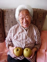 Portrait of senior woman holding pears while sitting on sofa