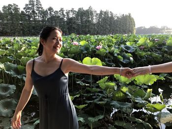 Cropped image of friend holding woman hand against plants