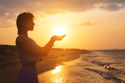 Portrait of a young woman in the form of a silhouette and hands holding the sun. sunset over the sea