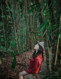 Side view of woman sitting on rock in forest