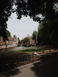 Footpath by canal and buildings against sky