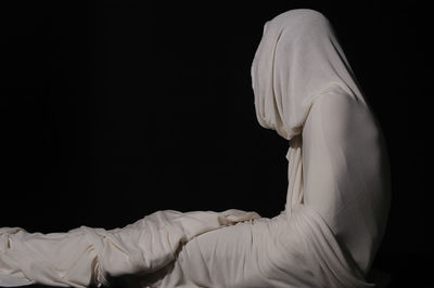 Person wrapped in white fabric against black background