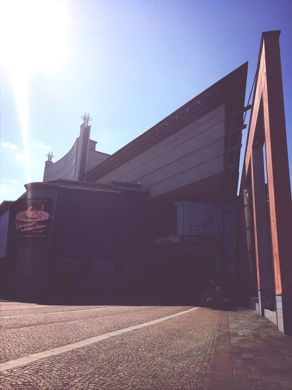 architecture, built structure, building exterior, sky, sunlight, clear sky, street, the way forward, low angle view, outdoors, day, road, sunny, house, roof, city, shadow, no people, building, incidental people