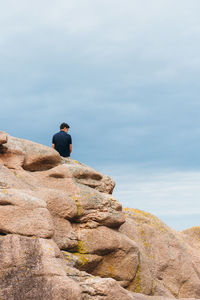 Rear view of man sitting on rock against sky