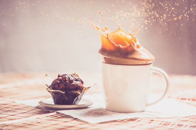 Coffee splashing in cup by muffin on table