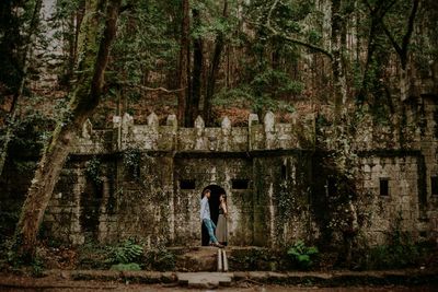 Side view of couple standing at old ruin in forest