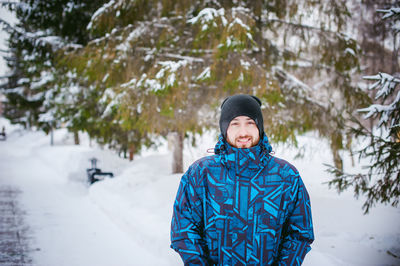 Portrait of young man smiling while standing against trees during winter