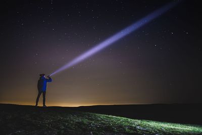 Man pointing flashlight on star field while standing on mountain