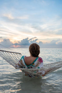 Rear view of woman swimming in sea against sky during sunset