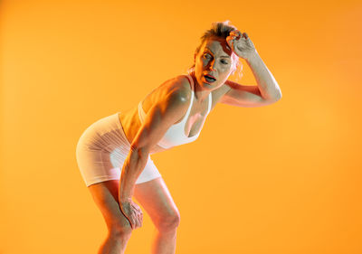 Low section of woman doing yoga against yellow background