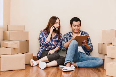 Young woman using phone while sitting on wooden floor