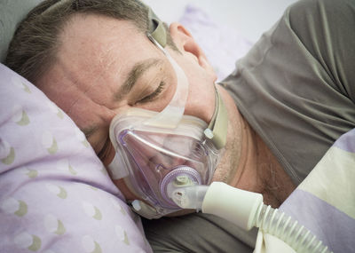 Close-up of patient wearing oxygen mask while lying on bed in hospital