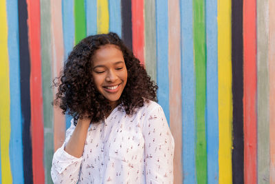 Portrait of smiling young woman standing against multi colored wall