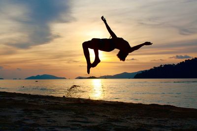 Silhouette man jumping on beach against sky during sunset