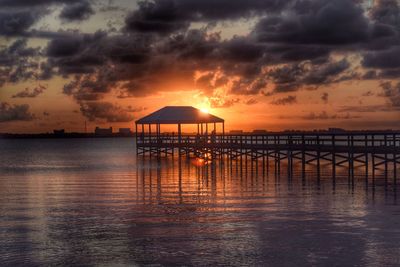 Gazebo on pier at sea against cloudy sky during sunset