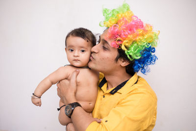 Father wearing wig carrying cute shirtless daughter against white background
