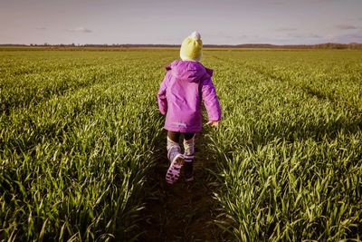 Rear view of girl in warm clothing walking on field against sky