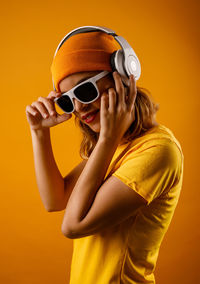 Woman wearing sunglasses standing against yellow background