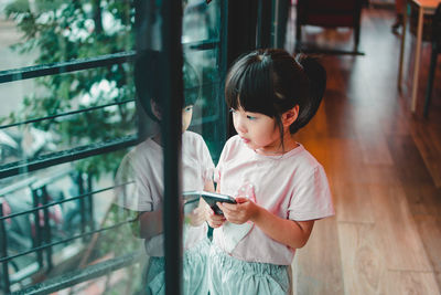 Girl looking at camera while standing by window