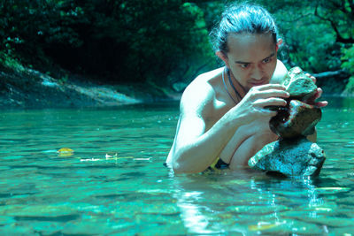 Shirtless man stacking stones in lake