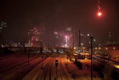 Illuminated railroad tracks in city against sky at night