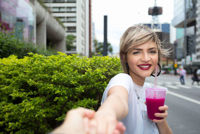 Portrait of a smiling young woman drinking glass outdoors