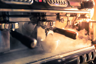 Close-up of machinery pouring coffee in cup at cafe