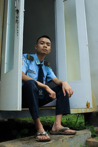 Portrait of young man sitting against wall