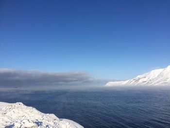 Scenic view of sea and snowcapped mountains against blue sky
