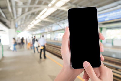 Cropped hand using blank phone at railroad station platform