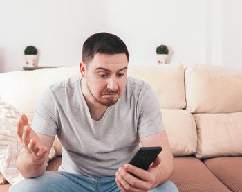 Young man using mobile phone while sitting on sofa at home