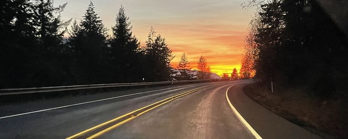 Empty road amidst trees against sky during sunset