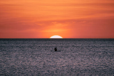 Man sitting on a paddleblard seeing the sunset 