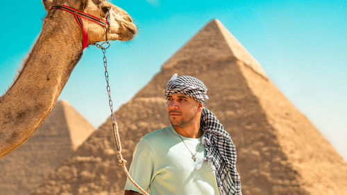 Full length of a man standing on sand at desert with the pyramids behind