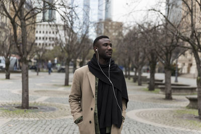 Young man looking away while standing on footpath in city